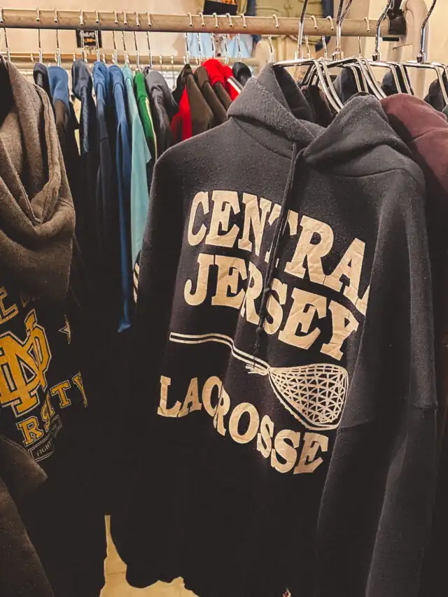 A black hoodie with "CENTRAL JERSEY LACROSSE" printed in large letters, hanging among various other colorful hoodies.