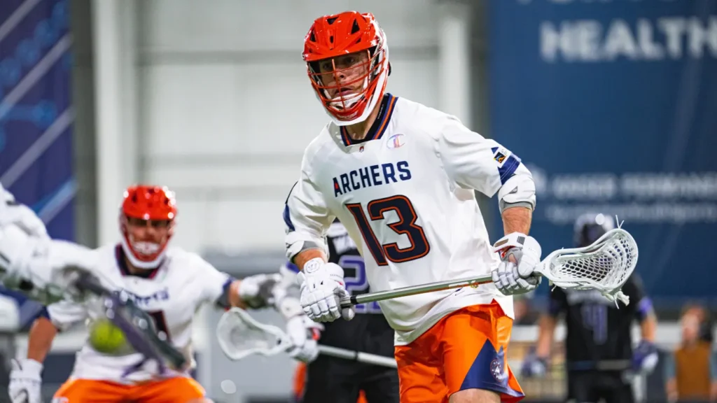 A lacrosse player in a white and orange uniform, number 13, prepares to pass the ball during a game.