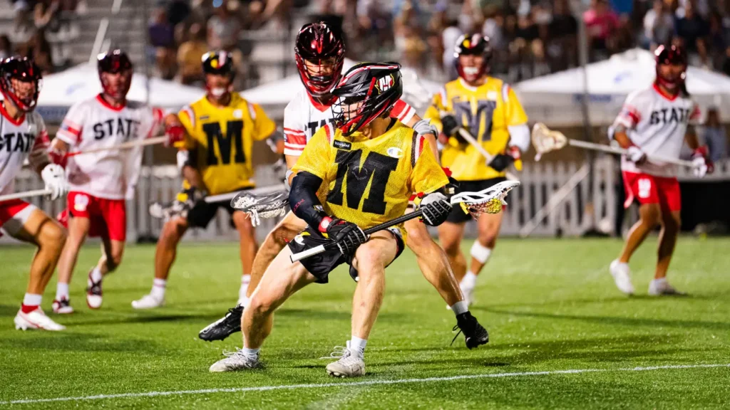 A lacrosse game in action, featuring players in yellow and red uniforms competing on a well-lit field.