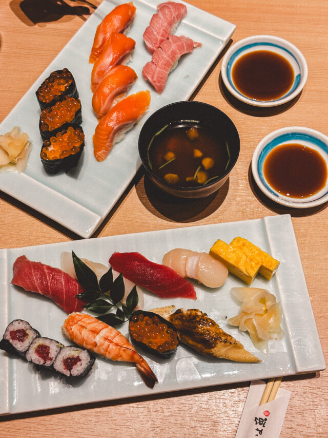 A beautifully arranged sushi platter featuring various types of sushi, sashimi, and a bowl of miso soup. Soy sauce and ginger accompany the meal.